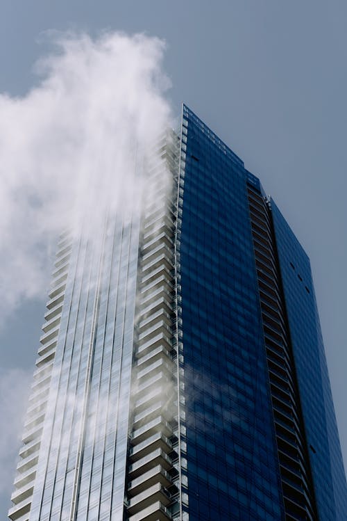 From below of contemporary multistory building exterior with balconies under blue sky with fluffy clouds in sunny town