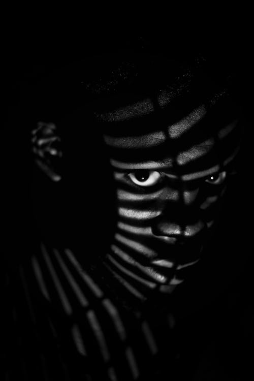 Black man in striped shadows in darkness