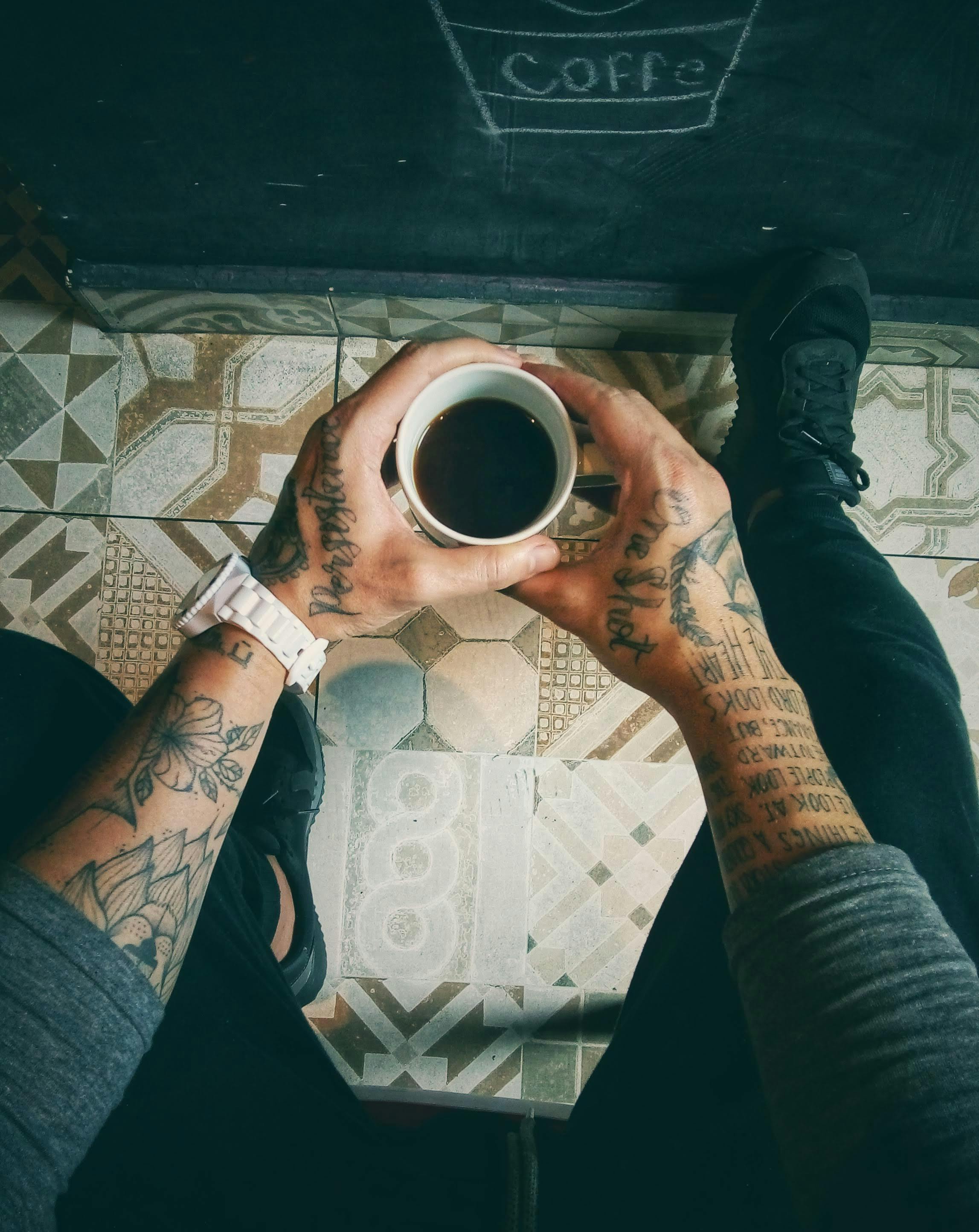 a tattooed person holding a cup of coffee