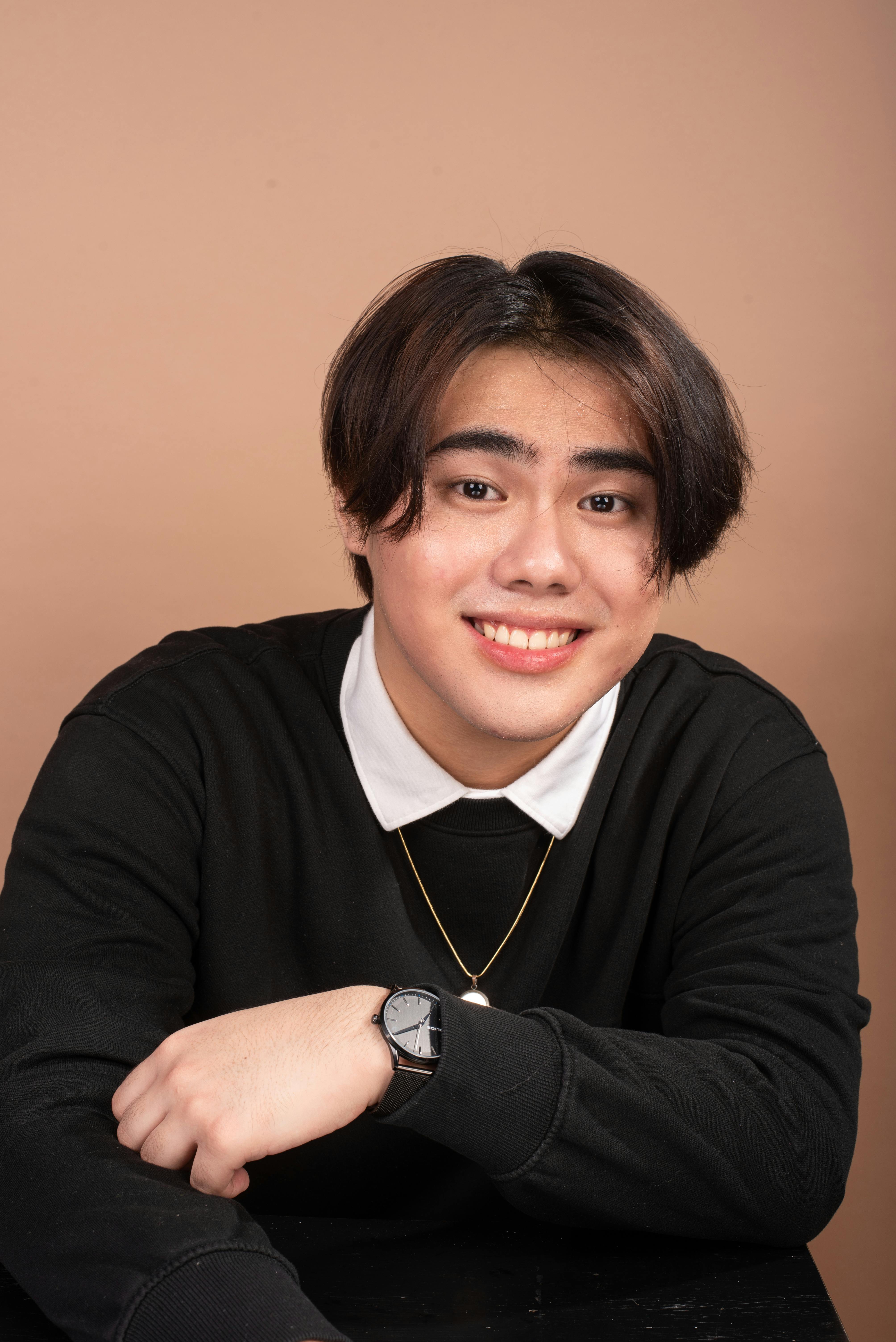 Portrait of a smiling young Asian man in a black sweater with a neutral background.