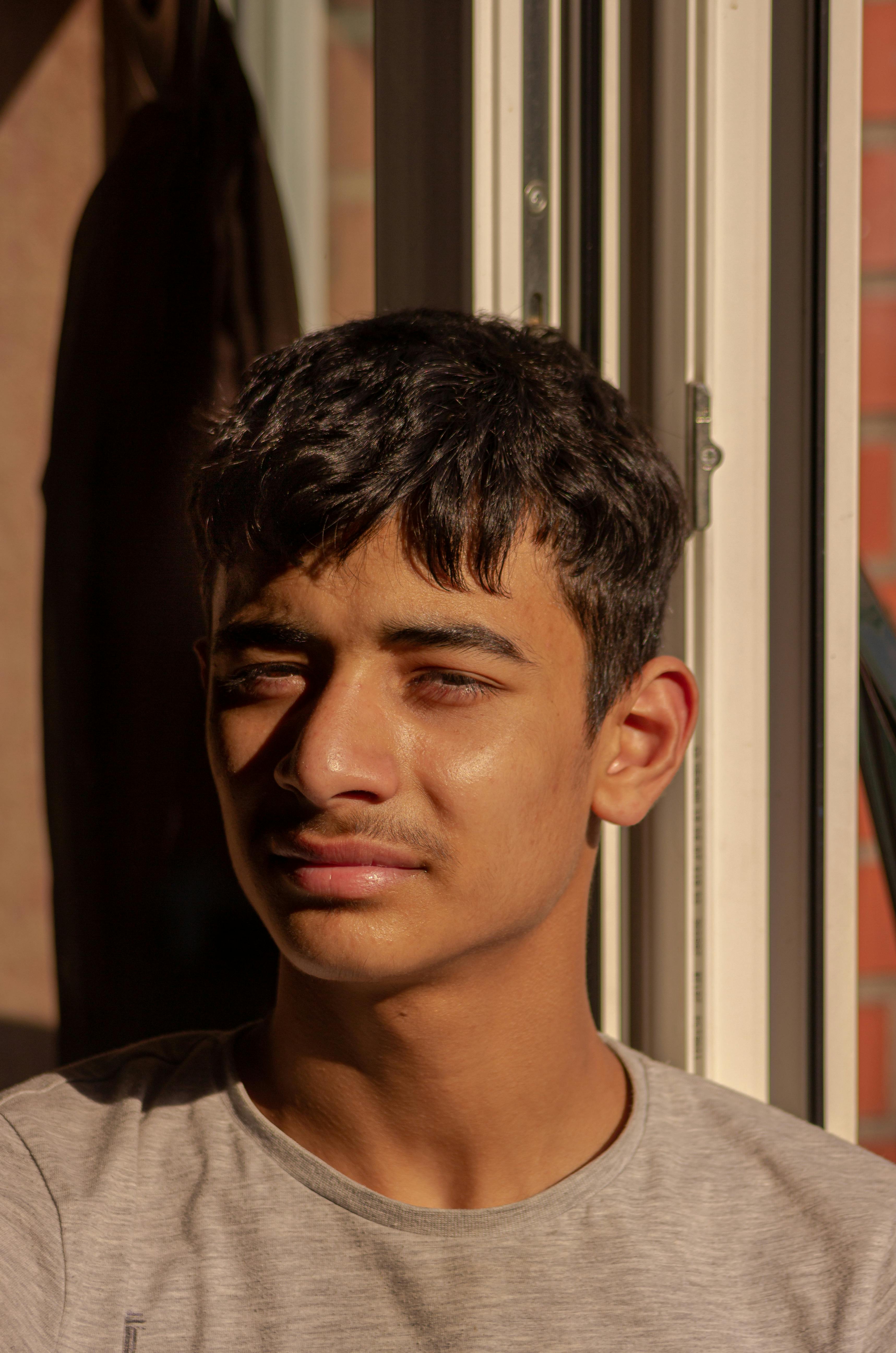 Portrait of a young man lit by warm sunlight from a window, creating a contemplative mood.
