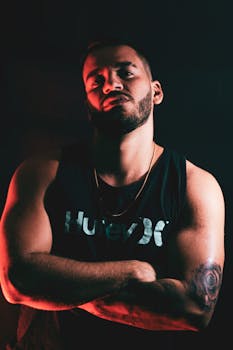 Portrait of a confident man with tattoos in dramatic lighting, wearing a tank top.