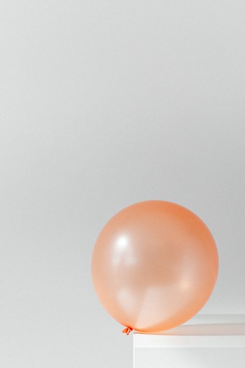 Free Simple minimalist photo of a single orange balloon on a white surface with a light gray background. Stock Photo
