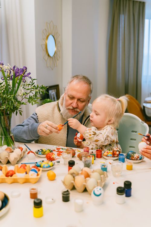 Free Grandfather and young girl enjoying Easter egg painting indoors together. Stock Photo