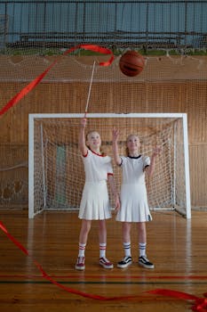 Two young girls practicing rhythmic gymnastics with ribbons in a sports hall, showcasing fun and fitness.