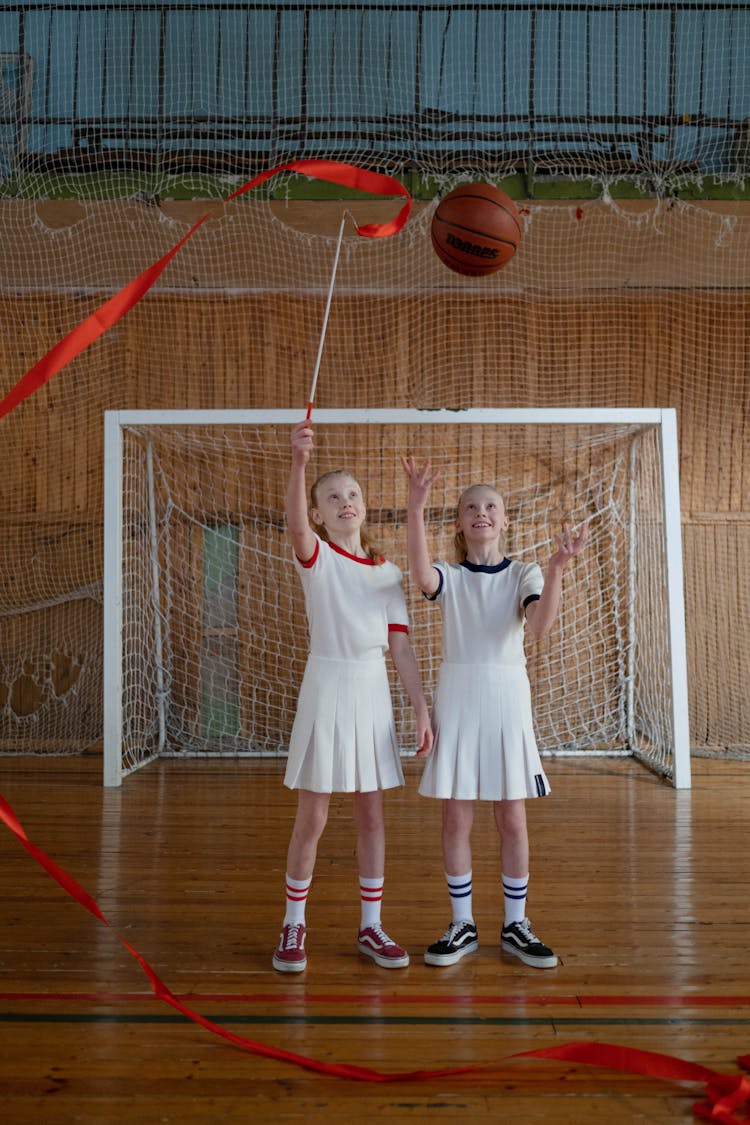 Girls Standing On The Wooden Floor Holding A Basketball And A Red Ribbon