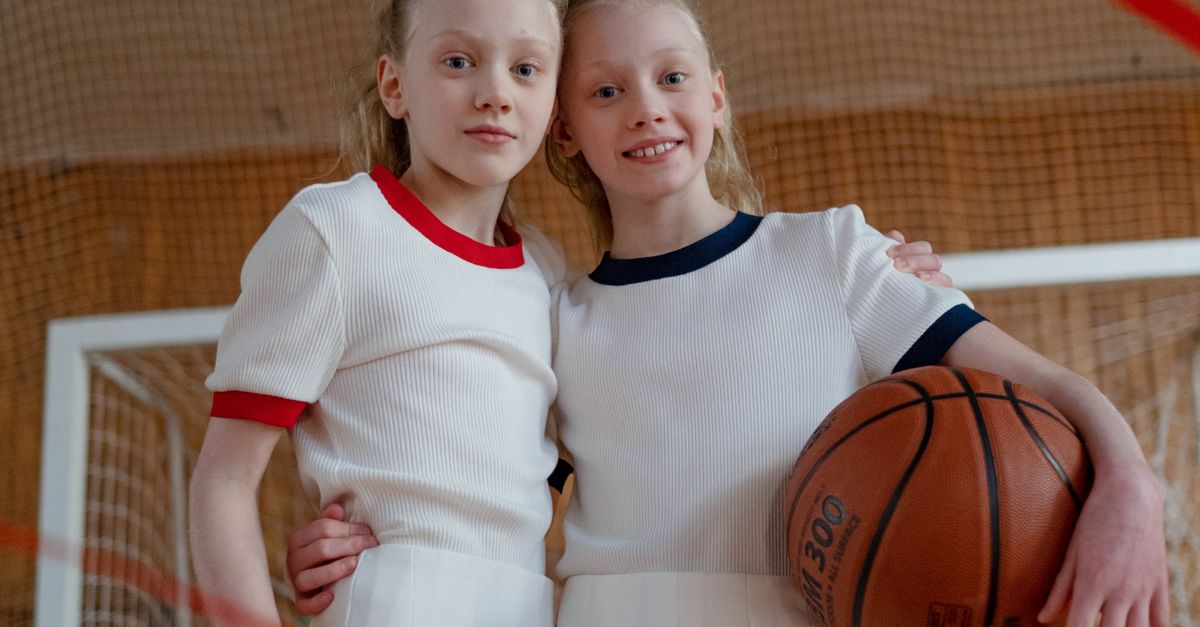 Rüyada Kardeşle Basketbol Oynamak - Rüya Tabiri ve Anlamı - Twin girls in matching sports uniforms holding a basketball indoors.