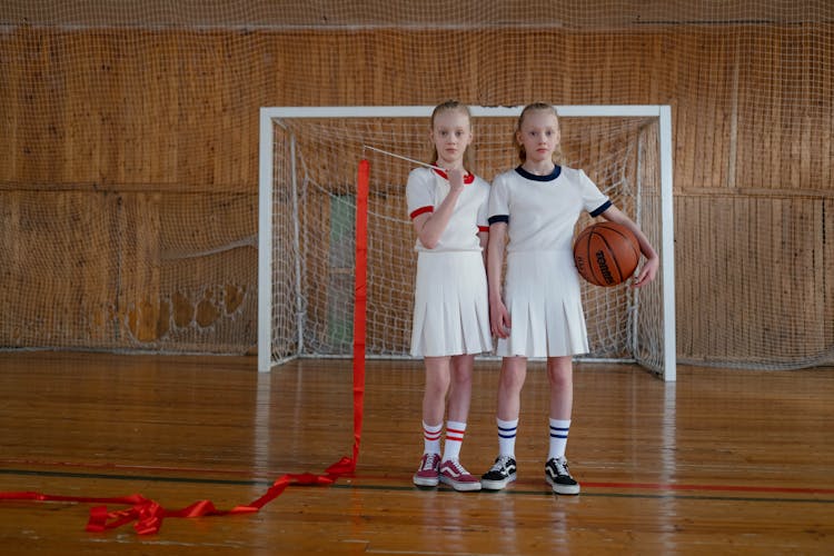 Girls Standing On The Wooden Floor Holding A Basketball And A Red Ribbon