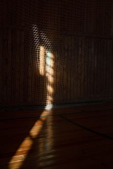 Artistic sunlight creates abstract patterns through a gym net, casting shadows on the floor.