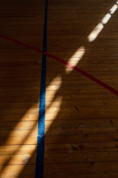 Sunlight creates contrasting shadows on a wooden gym floor with marked lines.
