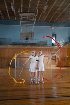 Two girls performing synchronized ribbon gymnastics in a sport hall.