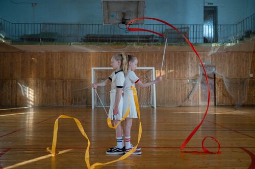 Free Two young gymnasts performing a ribbon routine indoors, showcasing their skills in rhythmic gymnastics. Stock Photo