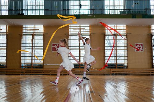 Free Young girls performing rhythmic gymnastics indoors with colorful ribbons. Stock Photo
