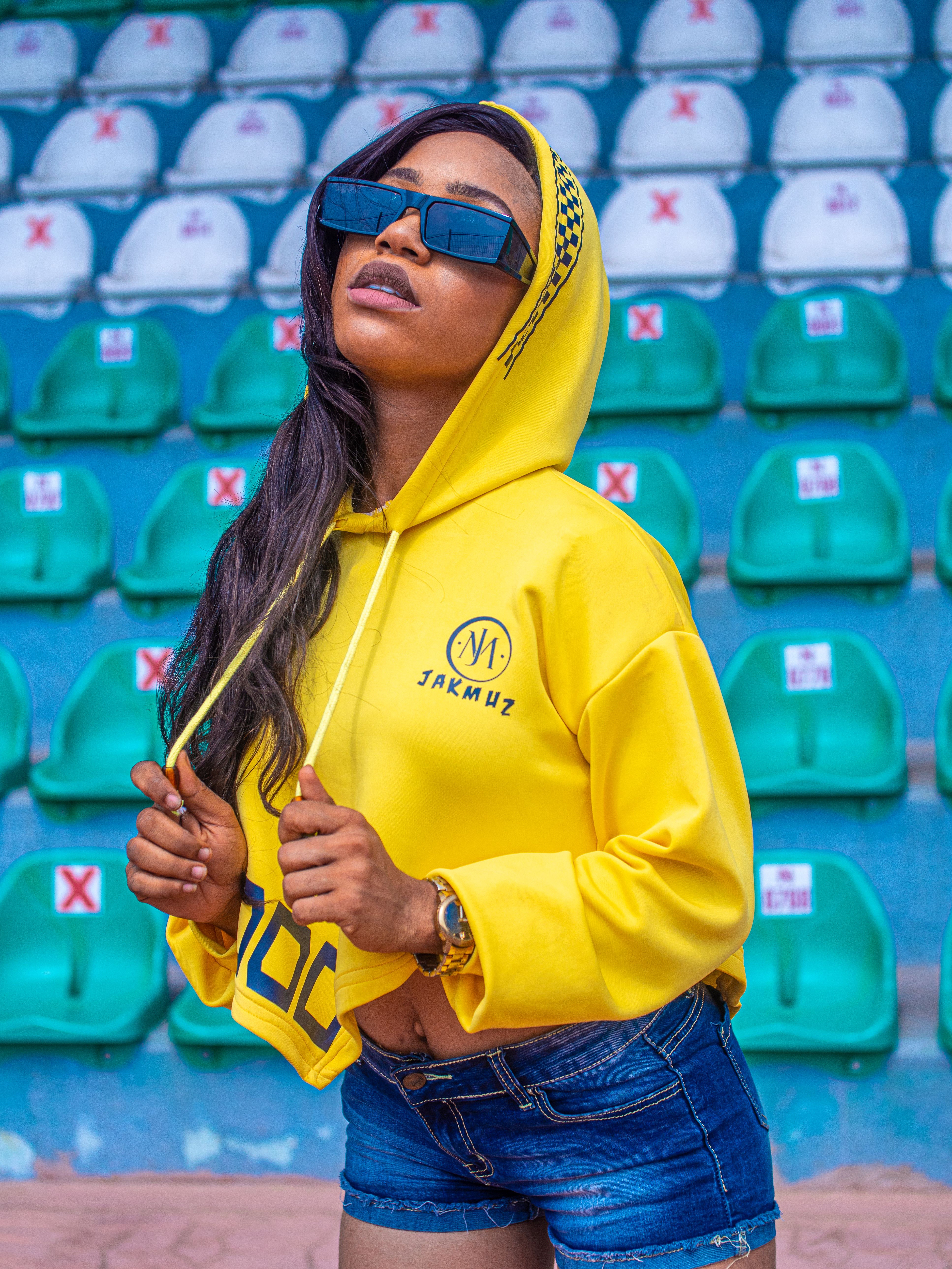 Stylish African woman poses in a vibrant yellow hoodie at an outdoor stadium.