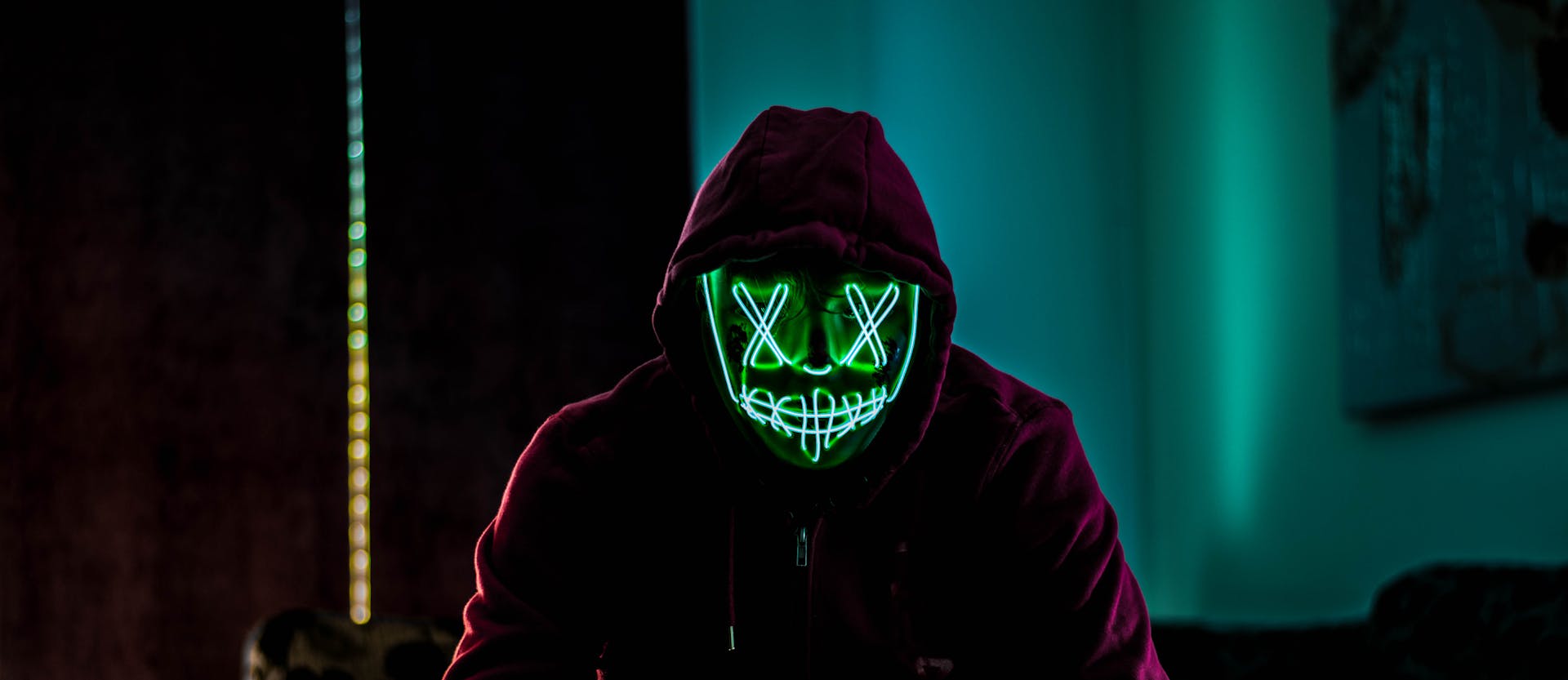 A person wearing a neon LED mask in a dark room, evoking mystery and intrigue.