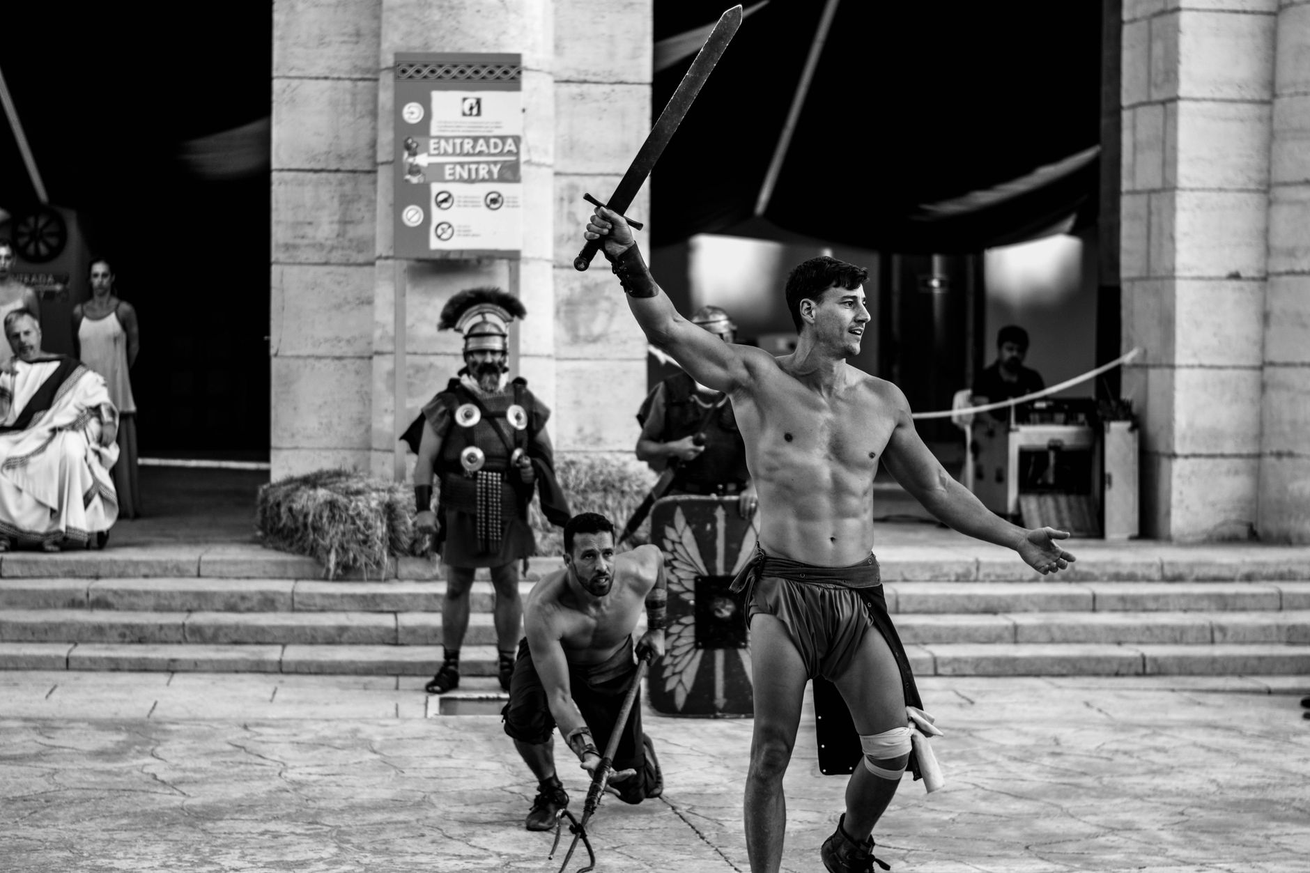 Dynamic scene of men reenacting a gladiatorial fight with swords, showcasing ancient Roman culture in grayscale.