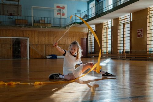 Free Child performing rhythmic gymnastics with ribbon in a sunny gym. Stock Photo