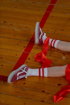 Close-up of legs in sneakers and ribbons on a gym floor, showcasing casual style.