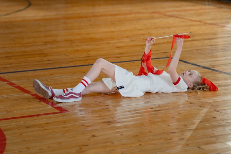 Girl In Sports Uniform Lying Down On Wooden Flooring