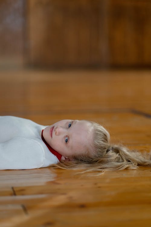 Shallow Focus Photo of a Girl in White Top Lying Down on Wooden Flooring