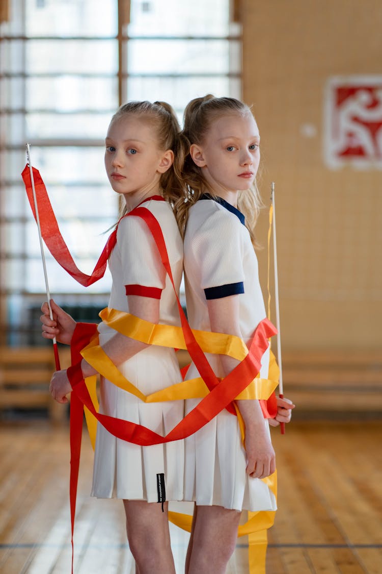 Two Female Gymnasts In Sports Uniform Holding A Ribbon