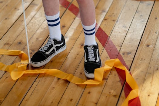 Child's sneakers and gymnastics ribbon on a wooden gym floor; a vibrant, indoor sports setting.