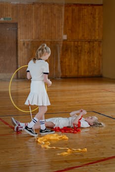 Two young girls in uniforms playing with hoops and ribbons in a gym hall.