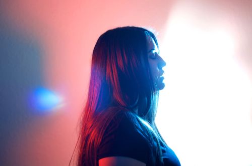 Free A woman in a studio with her eyes closed, illuminated by creative red and blue lighting. Stock Photo
