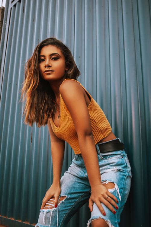 Free Trendy young woman posing against a blue wall in vibrant fashion attire, showcasing urban style. Stock Photo