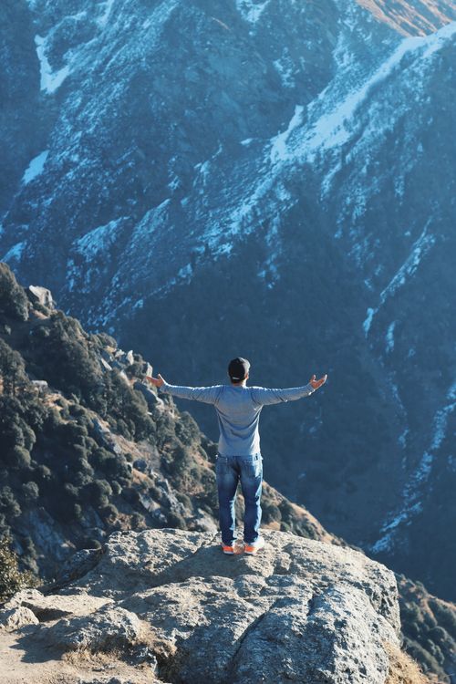 Free A man stands with open arms on a cliff, overlooking majestic mountains in India, embracing nature's beauty. Stock Photo