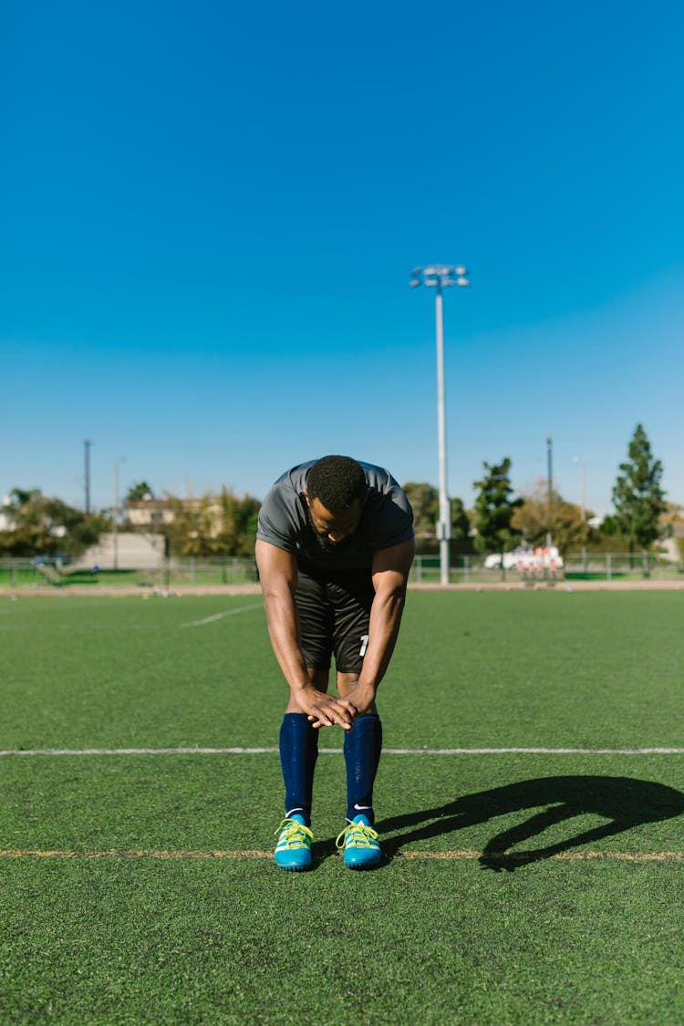 Man In Sportswear Stretching On Grass Field