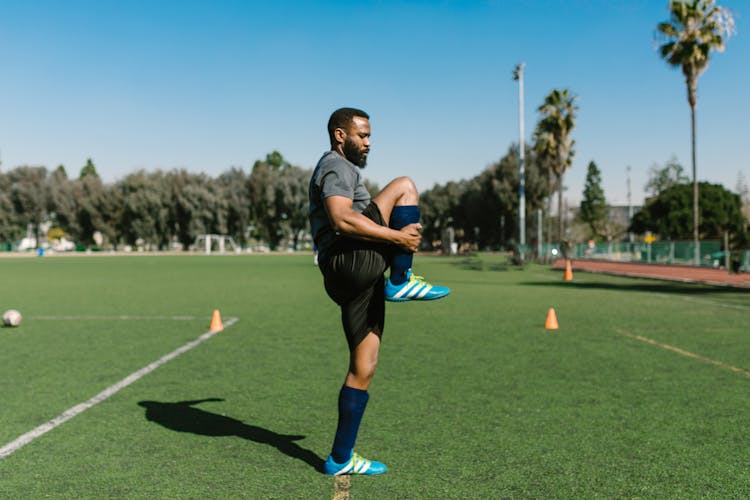 Man In Black Sportswear Stretching Legs On Grass Field