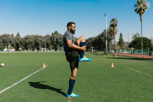 Free Athlete stretching on an outdoor football field in sportswear, preparing for training. Stock Photo