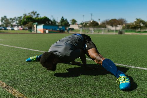 Free A dedicated athlete doing stretches on a grassy field, showcasing flexibility and strength. Stock Photo