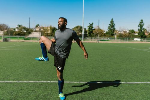 Free Athlete stretching on a soccer field during a sunny day, preparing for a workout. Stock Photo