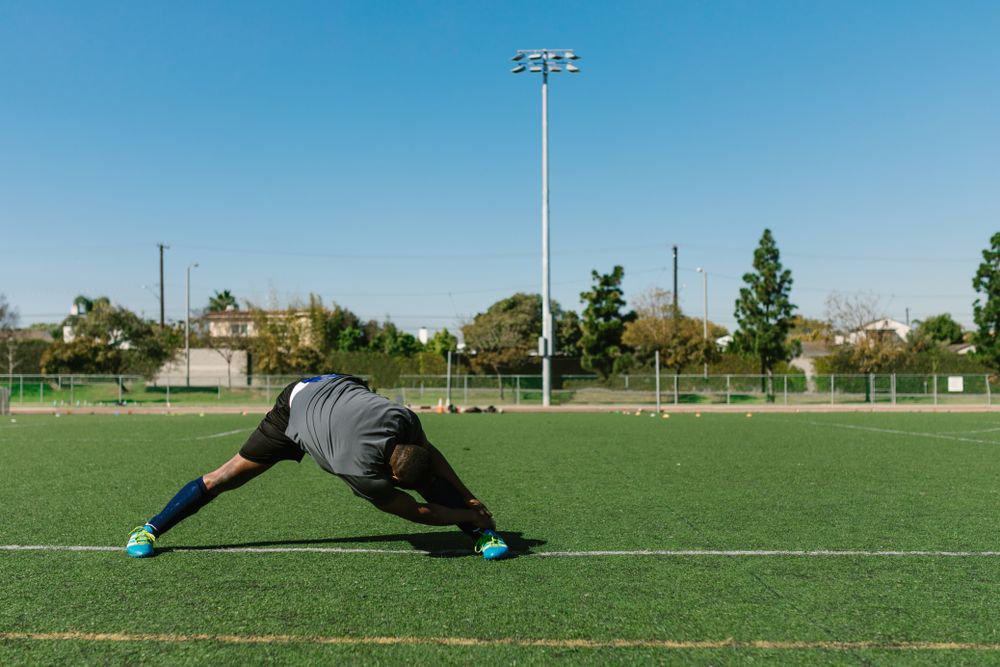 Athlete in a deep side lunge stretch on a playing field