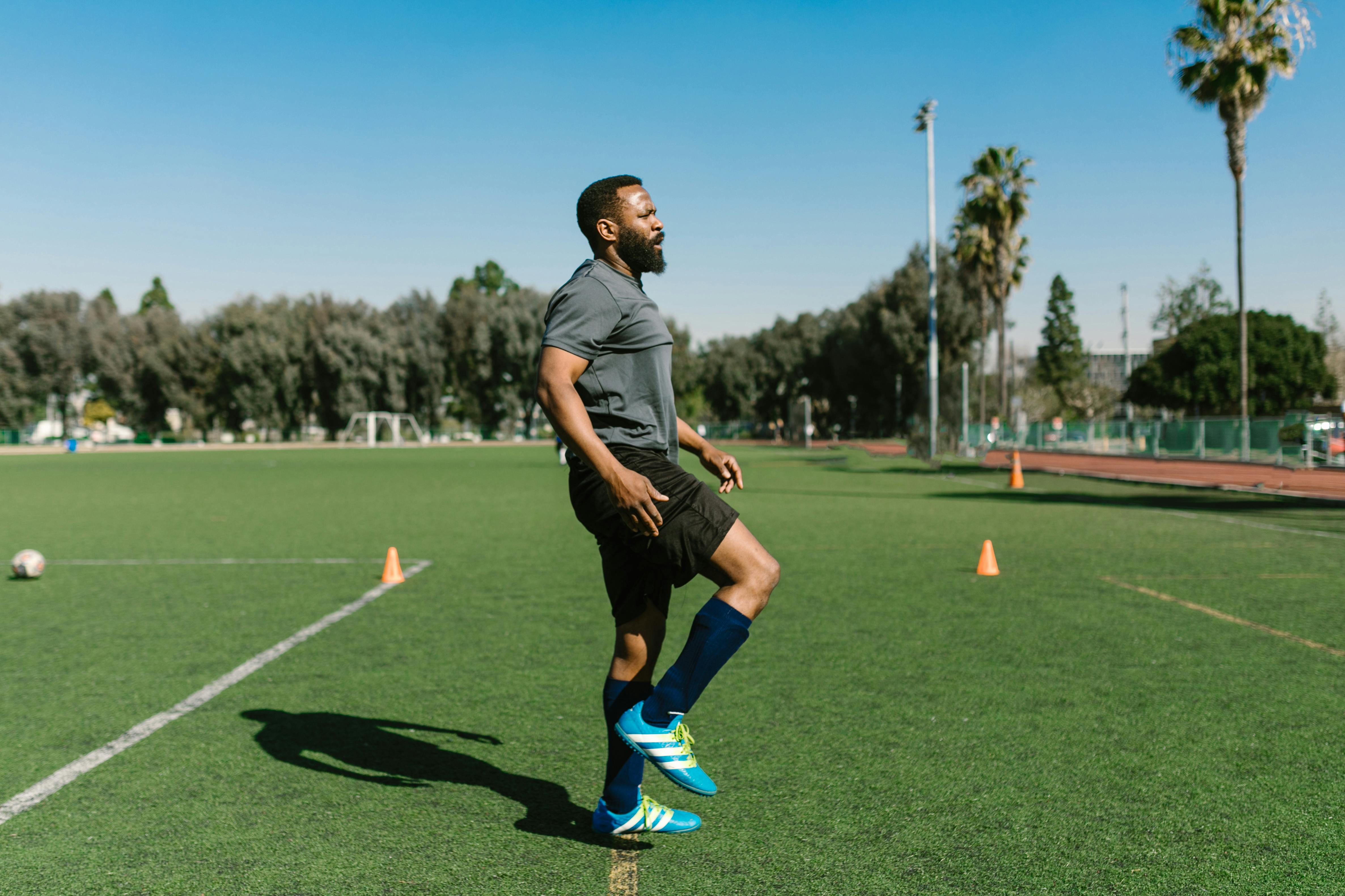 A soccer player warming up with exercises on a sunny day at an outdoor field.
