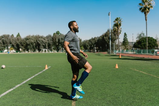 A soccer player warming up with exercises on a sunny day at an outdoor field.