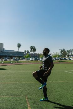 An athlete warms up on a sunlit soccer field, preparing for outdoor training.