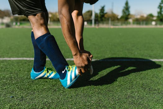 Athlete preparing with stretches on a green soccer field during a sunny day.
