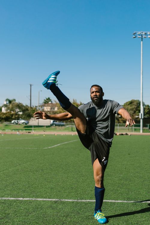 Free Athlete performs a high kick during a warm-up on a sunny soccer field. Stock Photo
