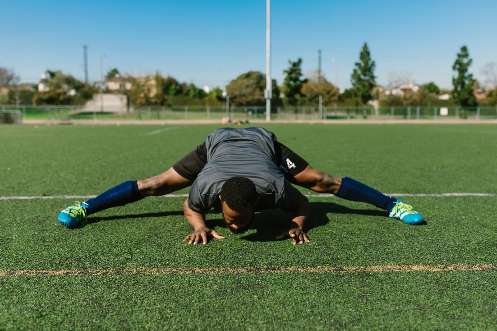 A focused football player warming up on a green training pitch at sunrise, cones and goalposts visible