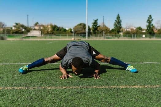 Athlete performing a stretching exercise on a sunny soccer field, focusing on fitness and flexibility.