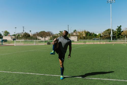 Free A man performs leg stretching exercises on a sunny soccer field, warming up for an outdoor workout. Stock Photo