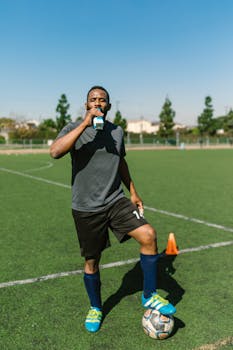 Athlete taking a break and hydrating on the soccer field during a sunny day.