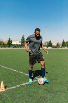 Athletic man practicing soccer skills on a sunny day outdoors on a green sports field.