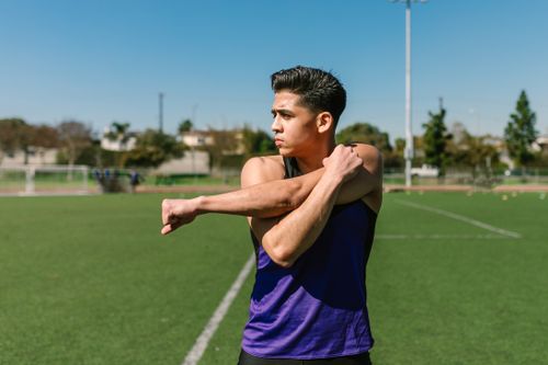 Free Asian man in sportswear stretching on a sunny field. Stock Photo