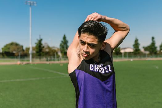 A young male athlete stretches on a sunny soccer field, preparing for practice.