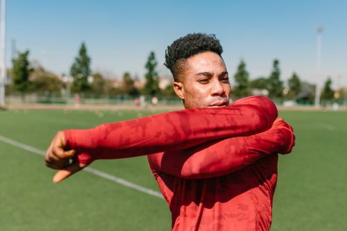 Free African American man warming up outdoors with a stretch in sportswear on a sunny day. Stock Photo