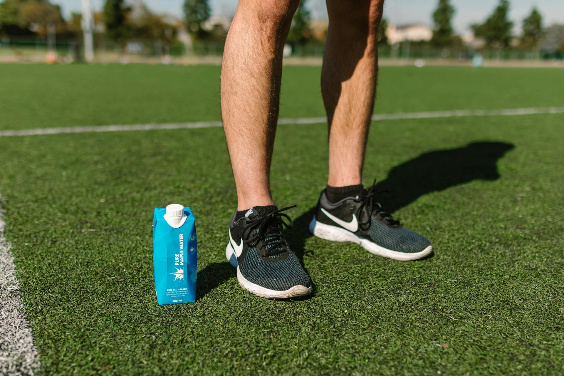 Male athlete's legs on a soccer field with Nike shoes and a drink pack on a sunny day.